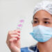 A person wearing a mask and holding a test tube Description automatically generated